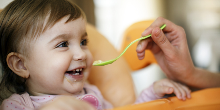 A smiling toddler gets a spoonful of porridge