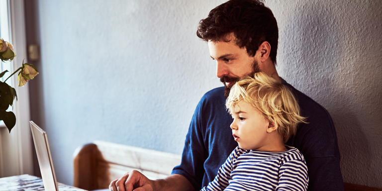 Un jeune père, avec son garçon sur les genoux, semble chercher des informations sur son ordinateur portable.
