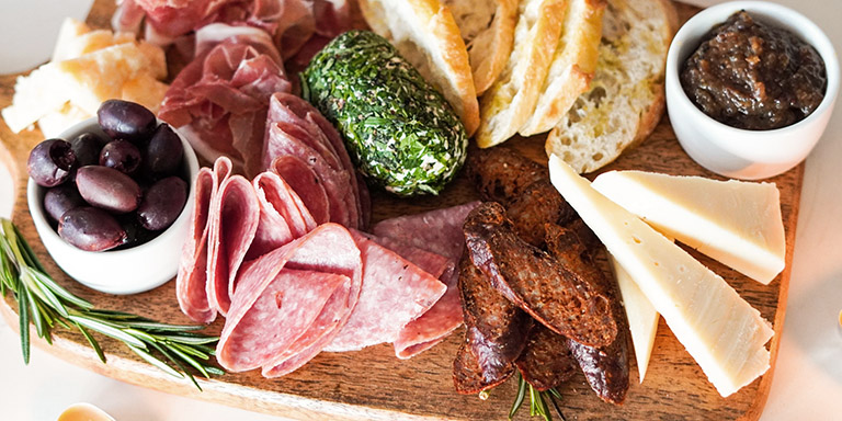 Apéro-Platte mit diversen Nahrungsmittel, darunter Fleisch, Käse, Brot, Oliven etc.
