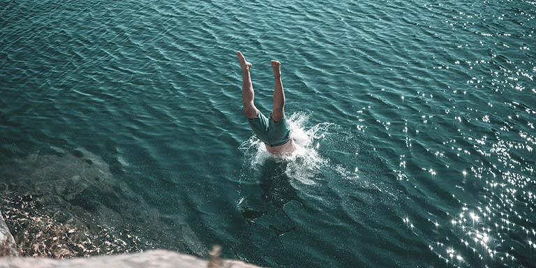 Ein Mann springt kopfüber von einer Klippe ins kalte Wasser