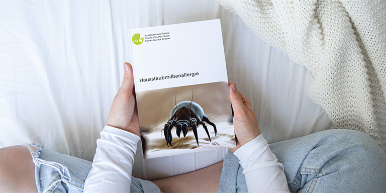 Eine Frau hält die Hausstaubmilbenallergie-Broschüre von aha! Allergiezentrum Schweiz in den Händen