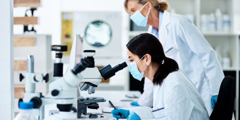 Eine Laborantin schaut dirch ein Mikroskop