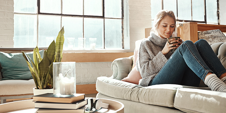 Une femme est assise sur un canapé et boit un thé.