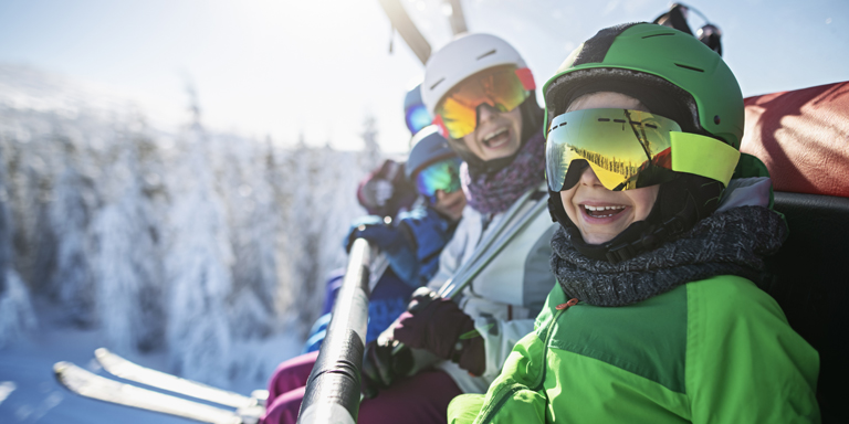 Des enfants en plein équipement de ski, par beau temps, sur un télésiège.