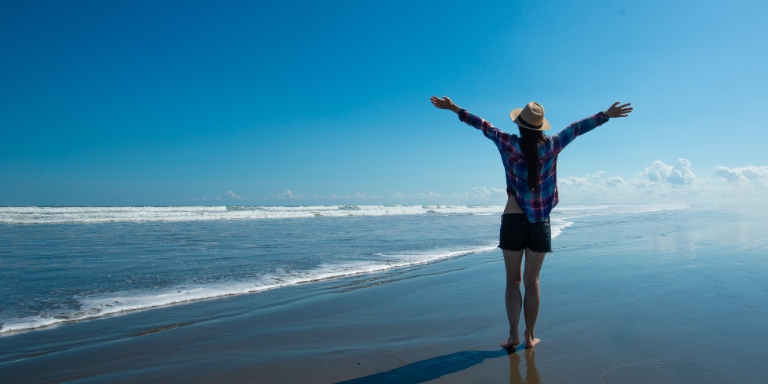 Une personne lève les bras en l'air sur une vaste plage