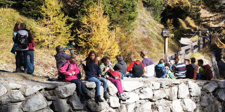 Ein Gruppe Kinder picknickt auf einer Trockensteinmauer sitzend.