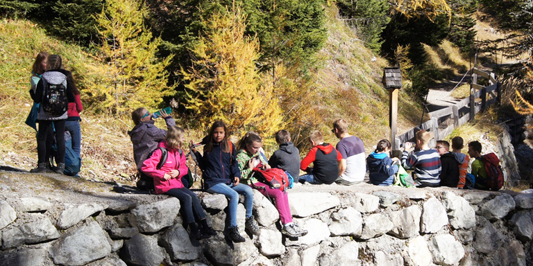 A group of children have a picnic sitting on a dry stone wall.