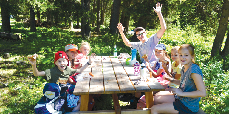 Fröhliche Kinder picknicken an Holztisch im Wald 