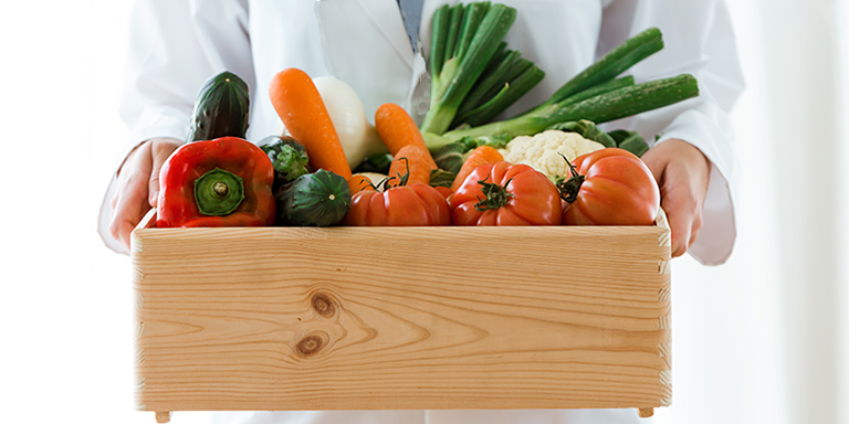 Ernährungsberaterin trägt eine Holzkiste mit frischem Gemüse.