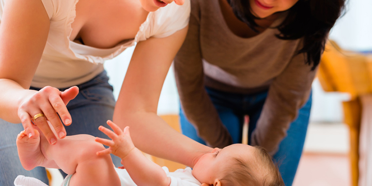 Zwei Frauen kümmern sich um ein Baby, das auf dem Wickeltisch liegt und strampelt.