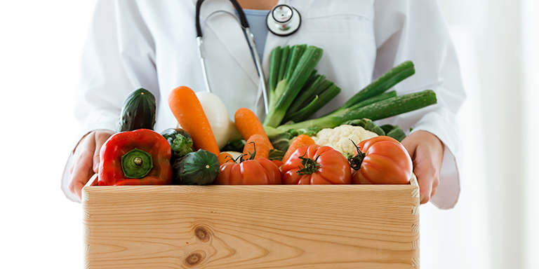 Une nutritionniste transporte une caisse en bois avec des légumes frais.