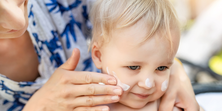 A mother puts cream on her toddler's face.
