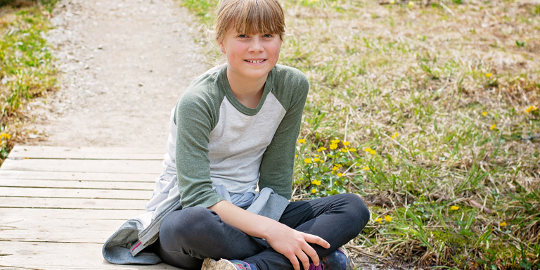 Une jeune fille est allongée dans l'herbe, la tête reposant dans ses mains, et regarde la caméra avec une expression taquine.